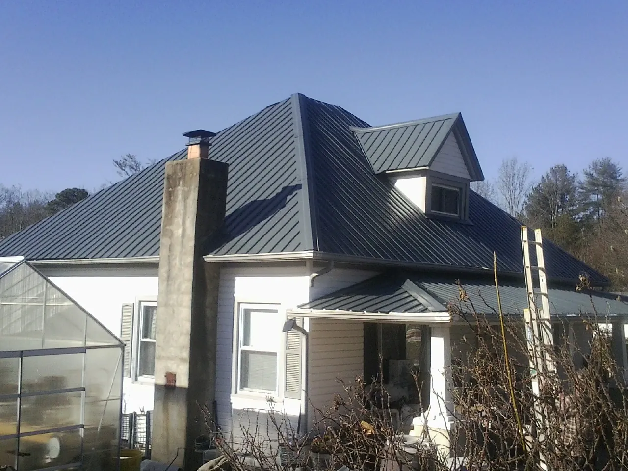 Dark blue standing seam metal roof on a white farmhouse with dormer — Slate & Tile Roof Repair by Roofing Brothers in Mango