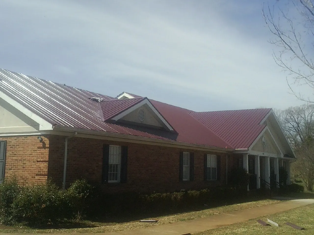 Red metal roof with gabled entries on a long brick building, from a Hail Damage Roof Repair job in Mango