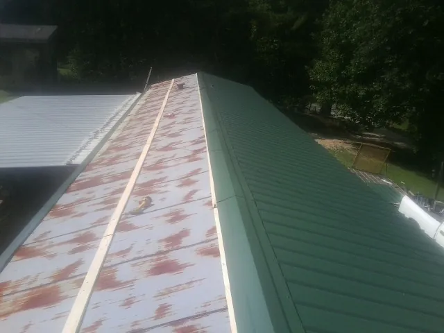 Old rusted panels beside newly installed green metal roofing — Wind Damage Roof Repair by Roofing Brothers in Mango